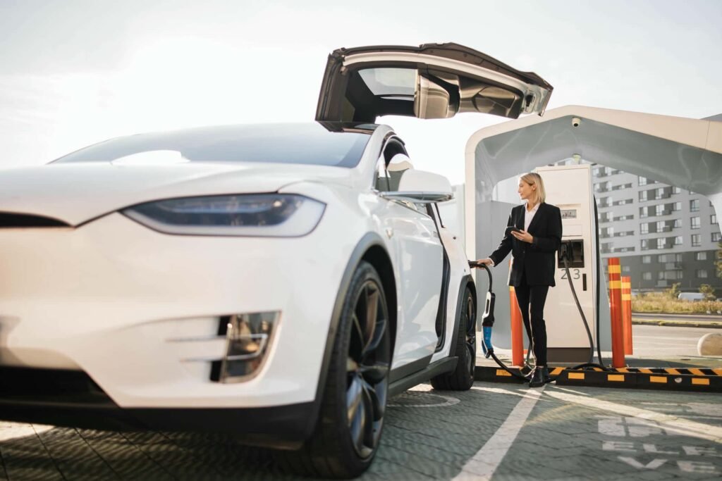 woman-using-smartphone-and-charging-car-outdoors-2023-11-27-04-50-08-utc - Tyre Shop Singapore | Tire Pte Ltd | tyre shop singapore | tire pte ltd