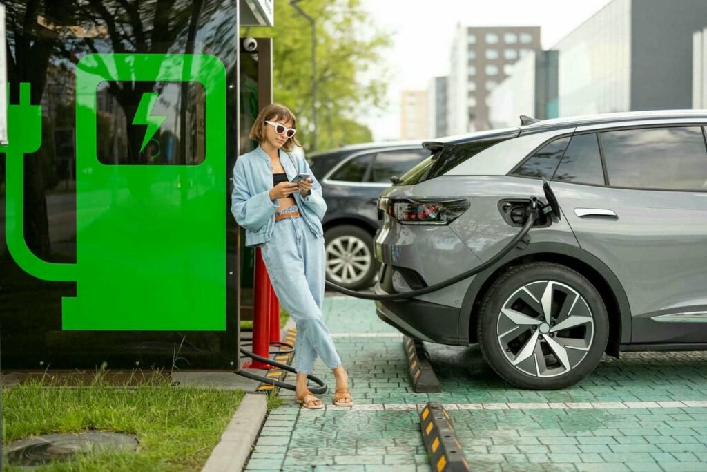 woman-with-a-smart-phone-waiting-for-her-electric-2023-11-27-05-29-53-utc - Tyre Shop Singapore | Tire Pte Ltd | tyre shop singapore | tire pte ltd