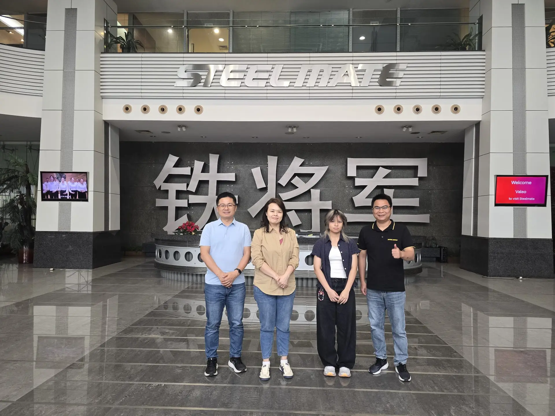 Five people stand in a modern lobby beneath a large steelmate sign and chinese characters on a dark wall behind them | tyre shop singapore | tire pte ltd | tyre shop singapore | tire pte ltd