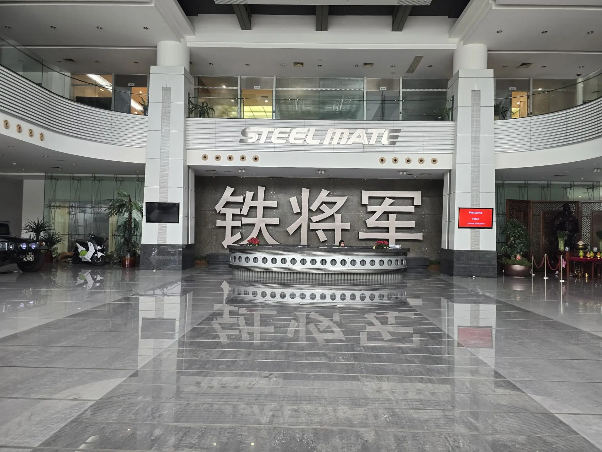 Spacious modern showroom lobby with a curved railing steel sign reading steelmate and a large chinese character backdrop behind a circular reception desk | tyre shop singapore | tire pte ltd | tyre shop singapore | tire pte ltd